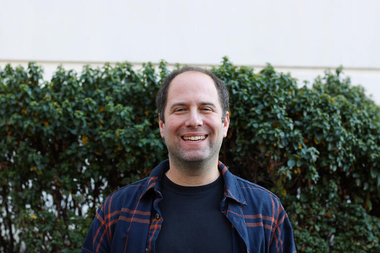 Man smiling wearing a plaid blue and orange shirt