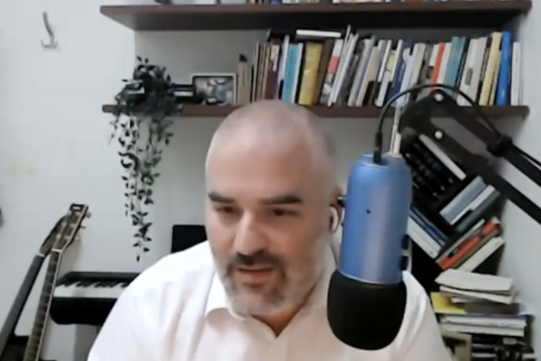 image of a bald man speaking into a microphone at his desk